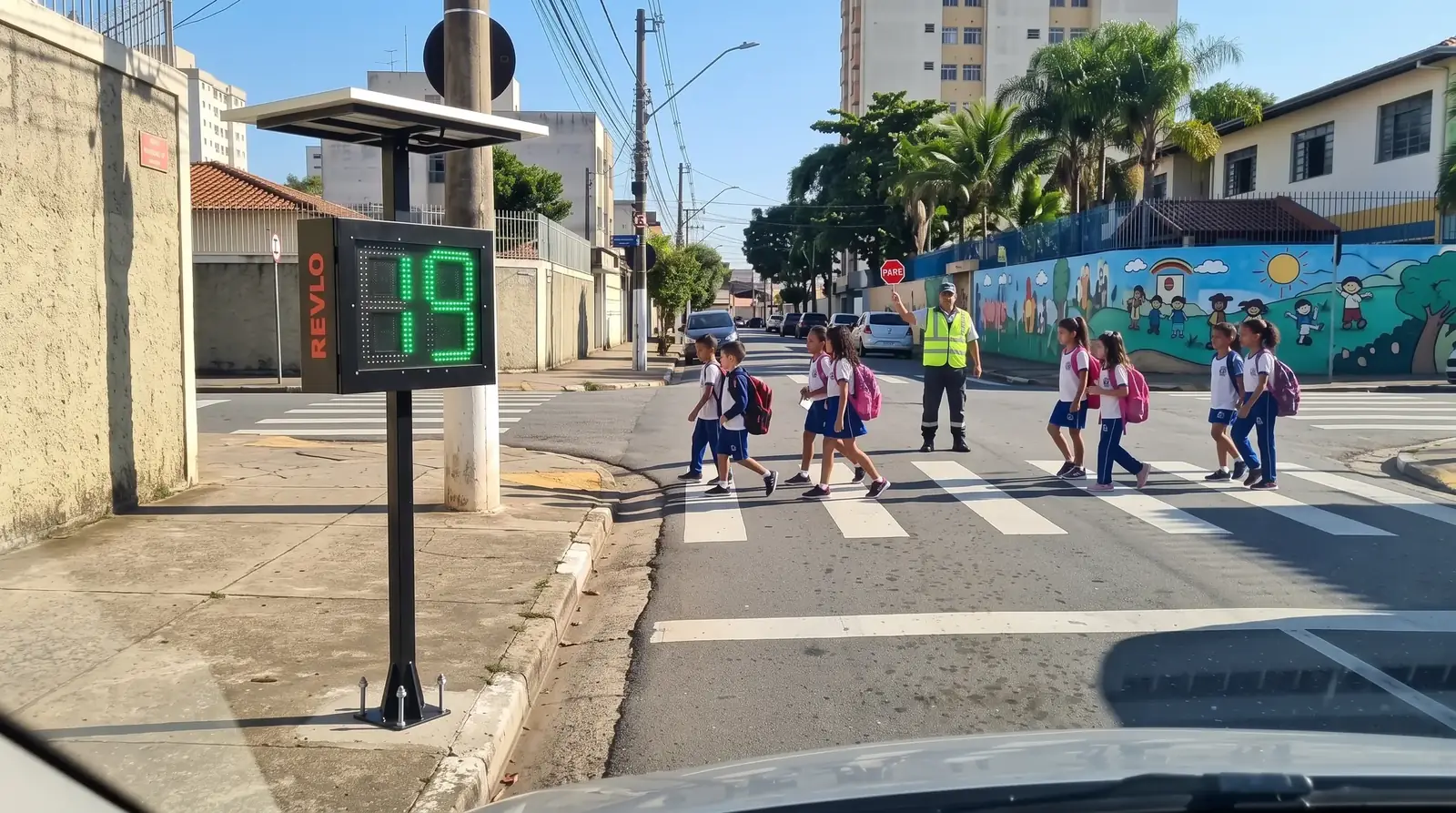 Lombada educativa Revlo na calçada de uma escola mostrando 19 enquanto crianças atravessam a faixa de pedestres